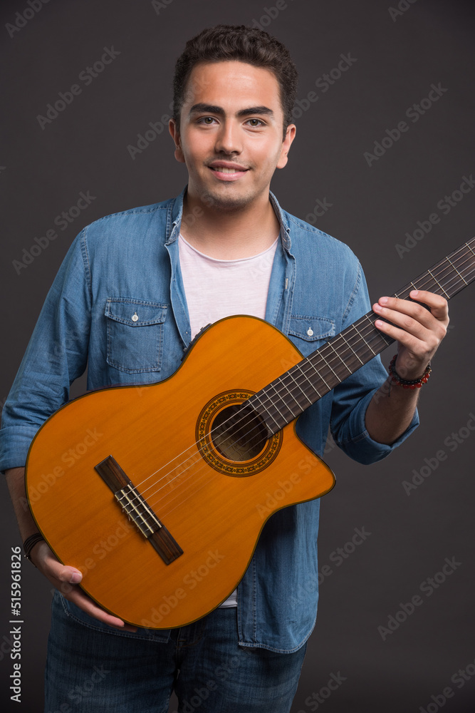 Obraz premium Brunette man with guitar smiling on dark background