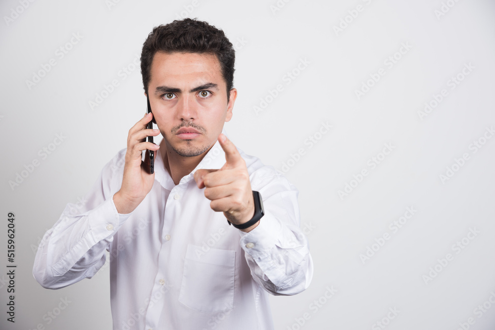 Businessman talking with cellphone and pointing at camera on white background Businessman talking with cellphone and pointing at camera on white background