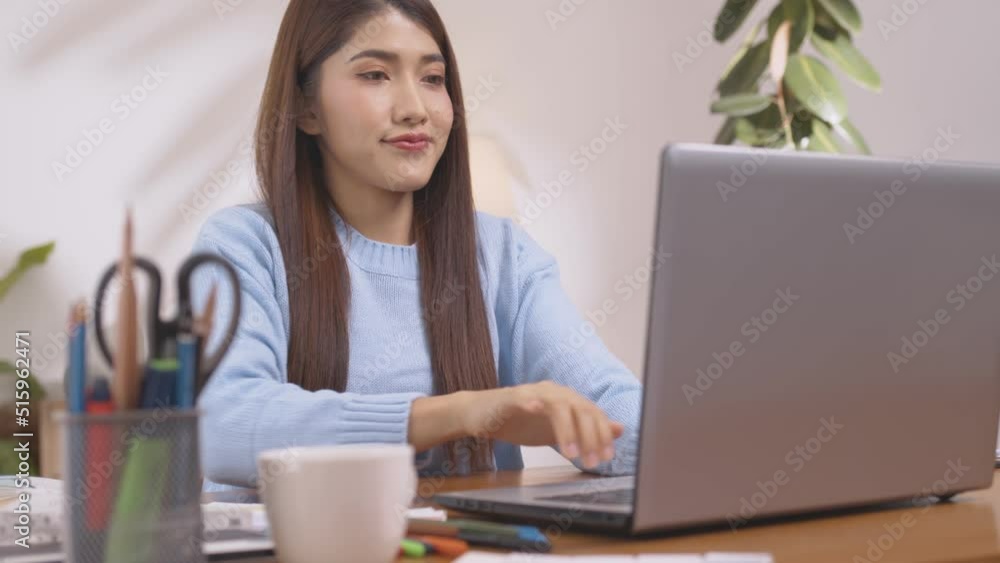 Enjoying the moment. At work, an Asian designer sits on a desk with his laptop, tablet, and documents, looking well and pleased. Enjoying the moment. At work, an Asian designer sits on a desk with his laptop, tablet, and documents, looking well and pleased.