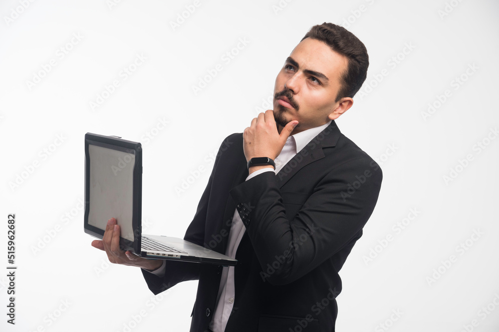A businessman in dress code holding a laptop and thinking A businessman in dress code holding a laptop and thinking