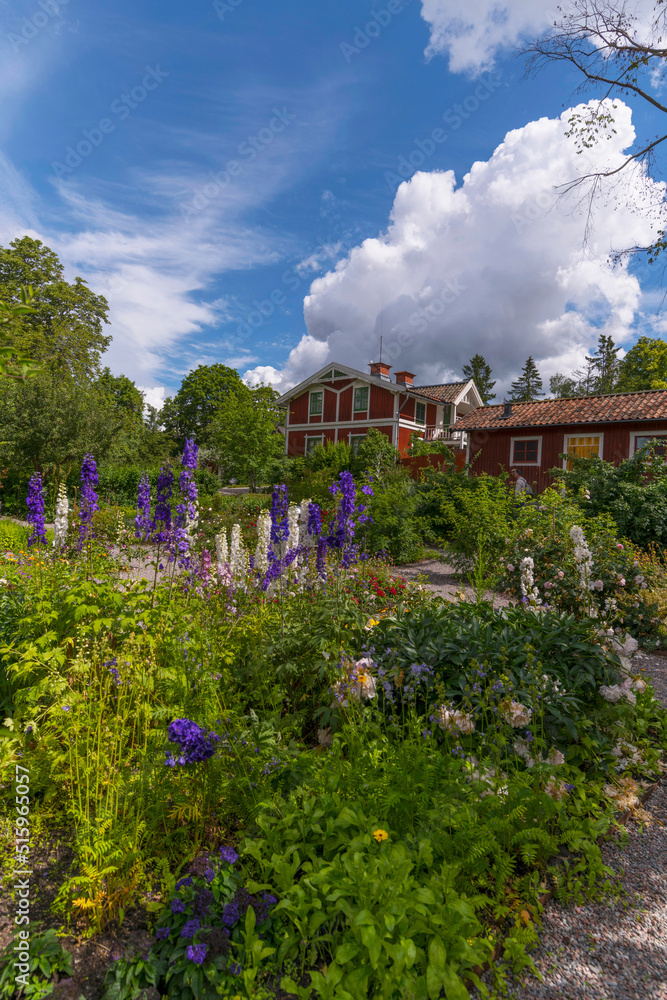 Landscape with old red wood houses and beautiful garden with flowers in a park a sunny summer day in Stockholm