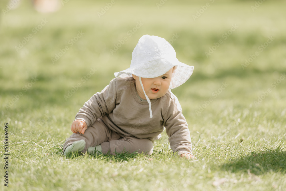A young 7-month child in the panama hat is playing in the meadow. An infant girl is crawling on the grass. A young 7-month child in the panama hat is playing in the meadow. An infant girl is crawling on the grass.