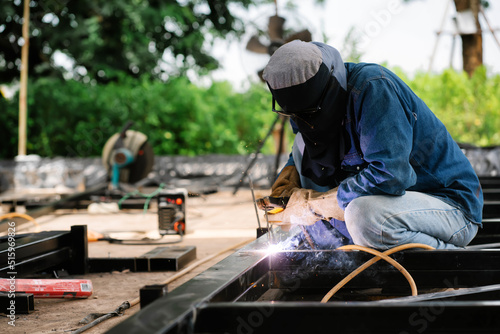 Steel welders welding large warehouse roof steel structures with electric welding tools.