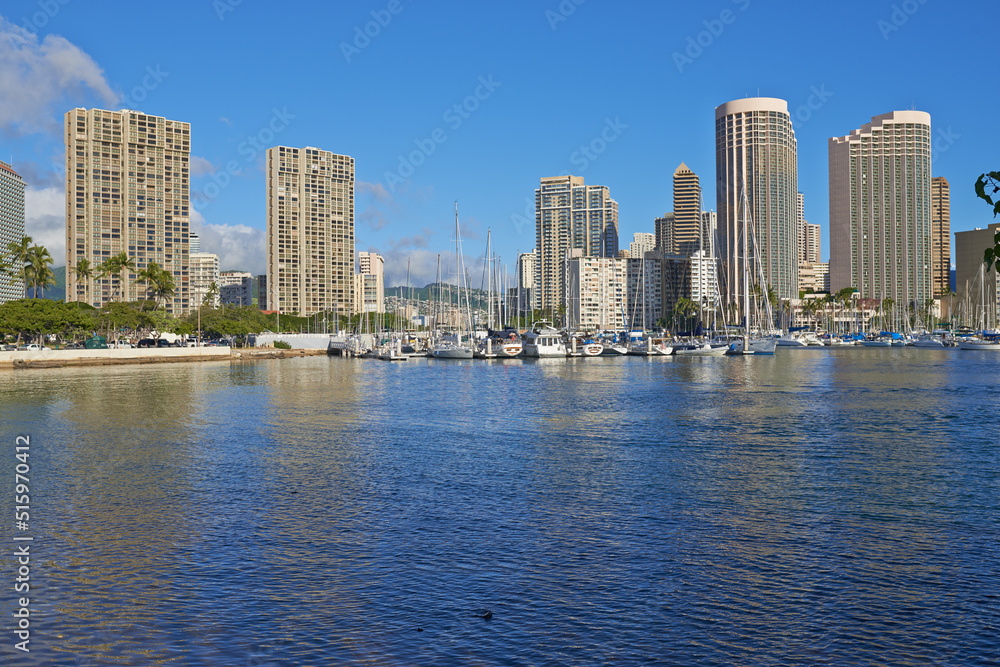 Apartments or business districts beside a harbour on a sunny day with a cloudy blue sky. A popular summer vacation tourist location in Hawaii. Luxury resort by the ocean in the USA on a tropical sea