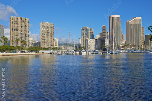 Apartments or business districts beside a harbour on a sunny day with a cloudy blue sky. A popular summer vacation tourist location in Hawaii. Luxury resort by the ocean in the USA on a tropical sea © SteenoWac/peopleimages.com