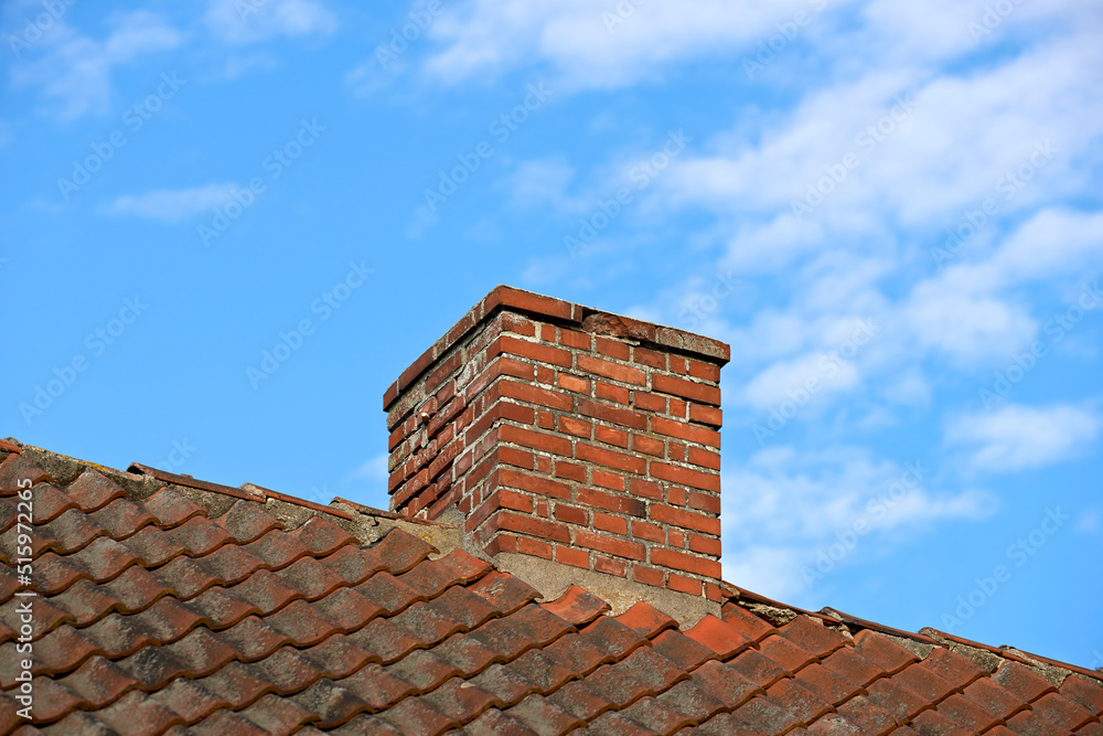 Red brick chimney designed on slate roof of a house building outside with blue sky background and copyspace. Exterior construction architecture of escape chute on rooftop for fireplace smoke and heat