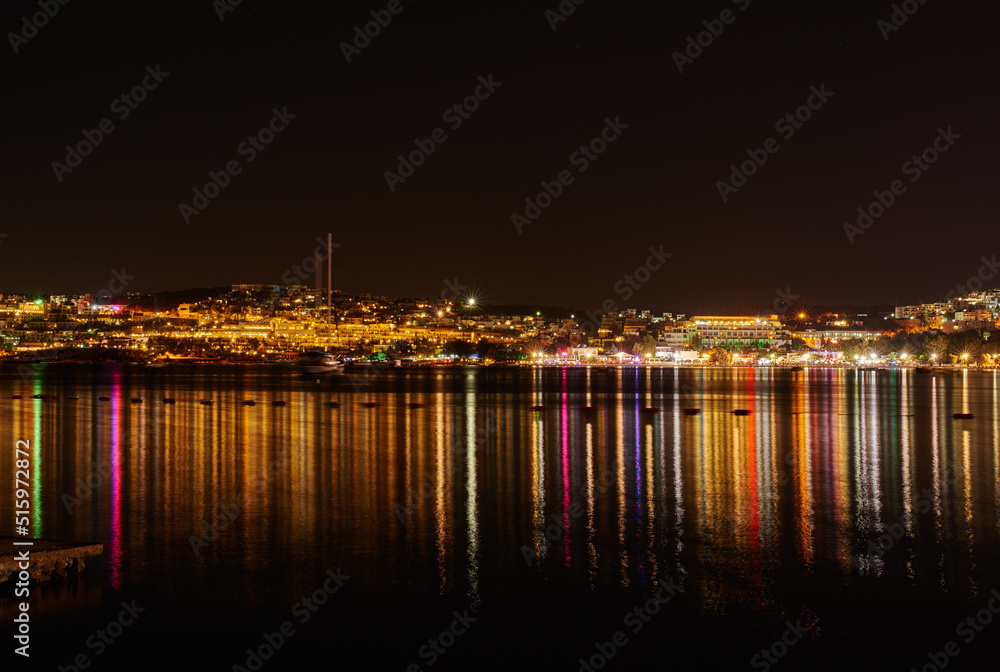City lights reflecting on water with dark sky copy space. River or lake at night with beach house light reflections on water surface. Colorful midnight skyscraper glowing in still water near a harbor
