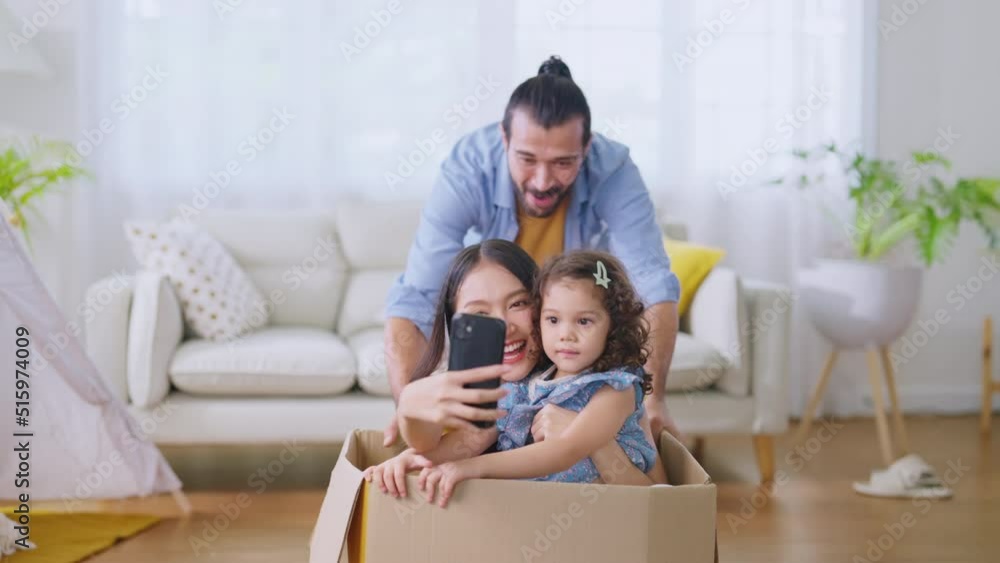 happiness father moving cardboard box with his little cute daughters and mother that sitting inside. Happy mother hand selfie on smartphone while laugh smile playing together joyful exited happiness father moving cardboard box with his little cute daughters and mother that sitting inside. Happy mother hand selfie on smartphone while laugh smile playing together joyful exited