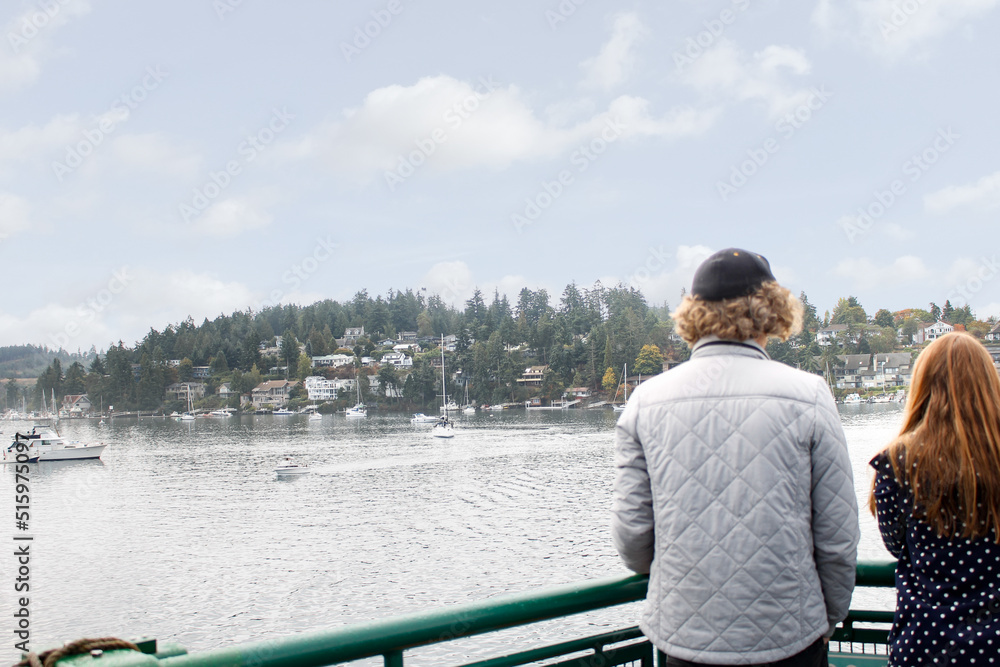 A view of a young couple standing at the railing of a ferry boat, looking out onto Friday Harbor Marina.