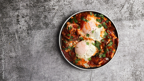 Shakshuka - eggs poached in spicy tomato pepper sauce on a round plate on a dark background. Top view, flat lay