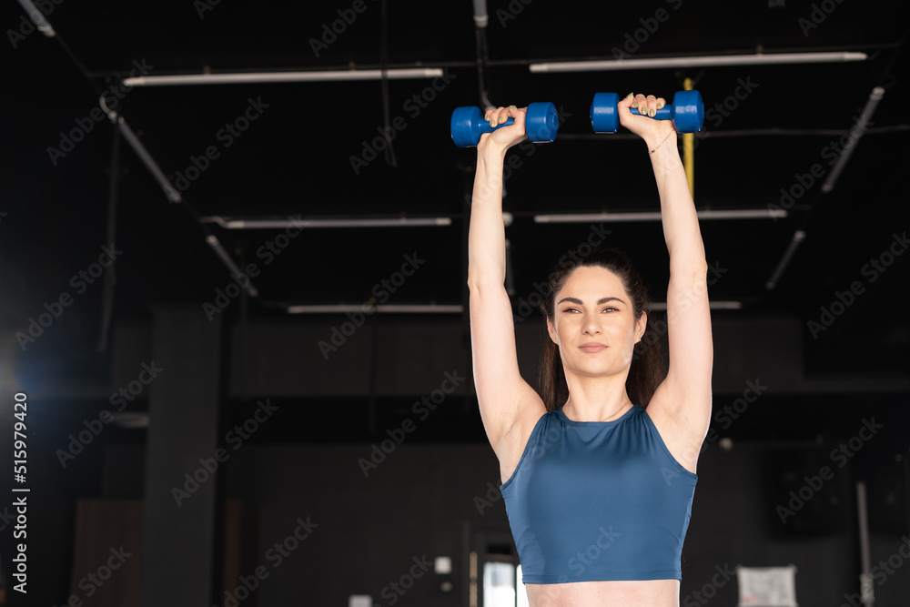 young fit woman lifting dumbbells on dark background building the arm muscles. fitness sports woman workout with dumbbells in gym. young fit woman lifting dumbbells on dark background building the arm muscles. fitness sports woman workout with dumbbells in gym.