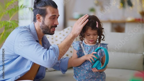 lively family father and daughter listen favourite song together,daddy is prepare headphone for her daughter while she is wonder and curious where the sound is come from in living room at home