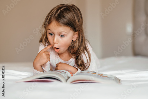 Fantasy literature. Emotional child girl read interesting book in bed. kid enjoy reading. Fantasy and fantastic. Developing child fantasy and imagination. Imaginary world. Fairy tale. Bedtime reading