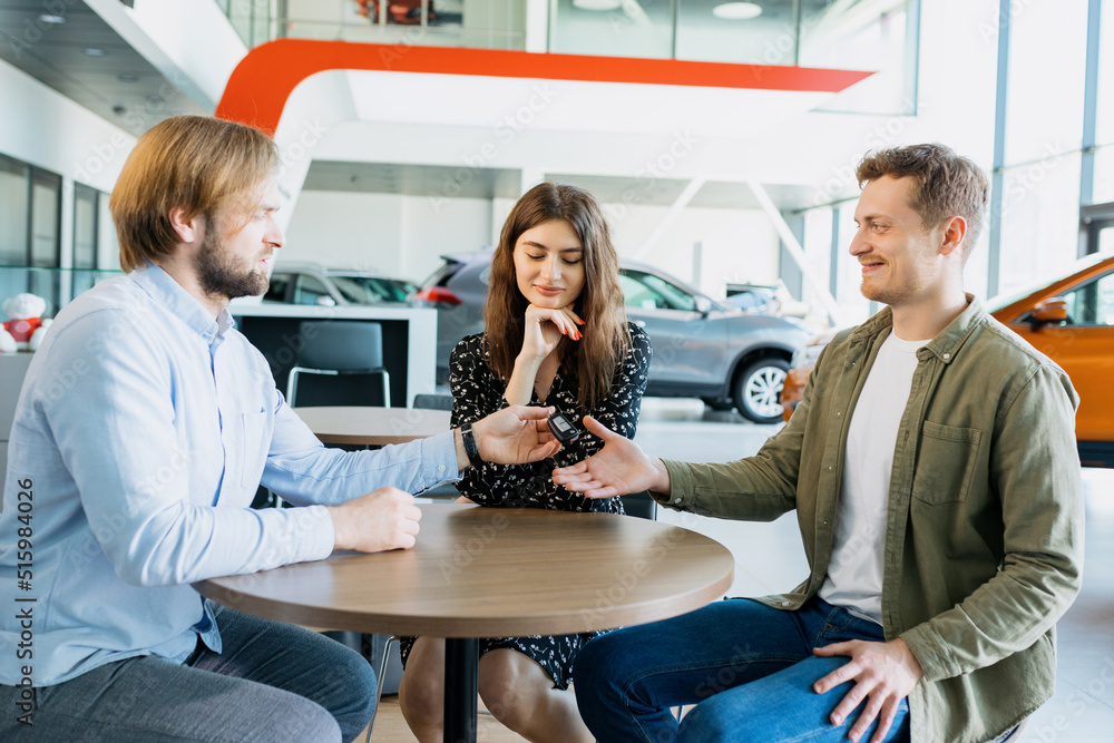 The manager of the dealership gives the keys to the new car to her husband and the wife is sitting next to him. Buying a family car. The manager of the dealership gives the keys to the new car to her husband and the wife is sitting next to him. Buying a family car.