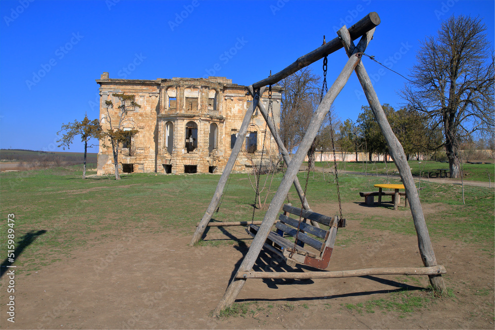 Fototapeta premium Wooden swing against the backdrop of an old abandoned estate.