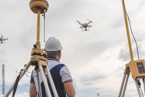A surveyor operating a drone to conduct topographic RTK or PPK aerial survey or photography of a site. A GNSS receiver is visible in front. photo