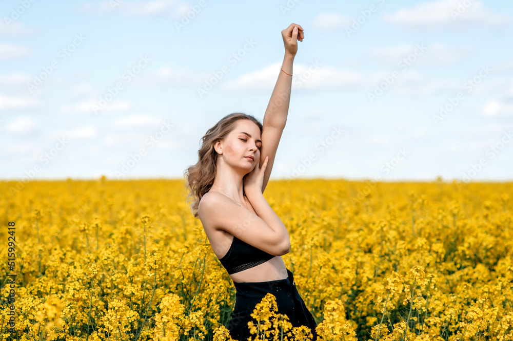 a girl in a black top and black trousers stands with her hand raised up in a yellow rapeseed field in spring a girl in a black top and black trousers stands with her hand raised up in a yellow rapeseed field in spring