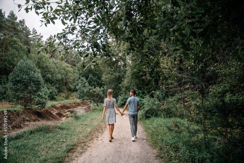 A guy and a girl holding hands are walking in the spring forest