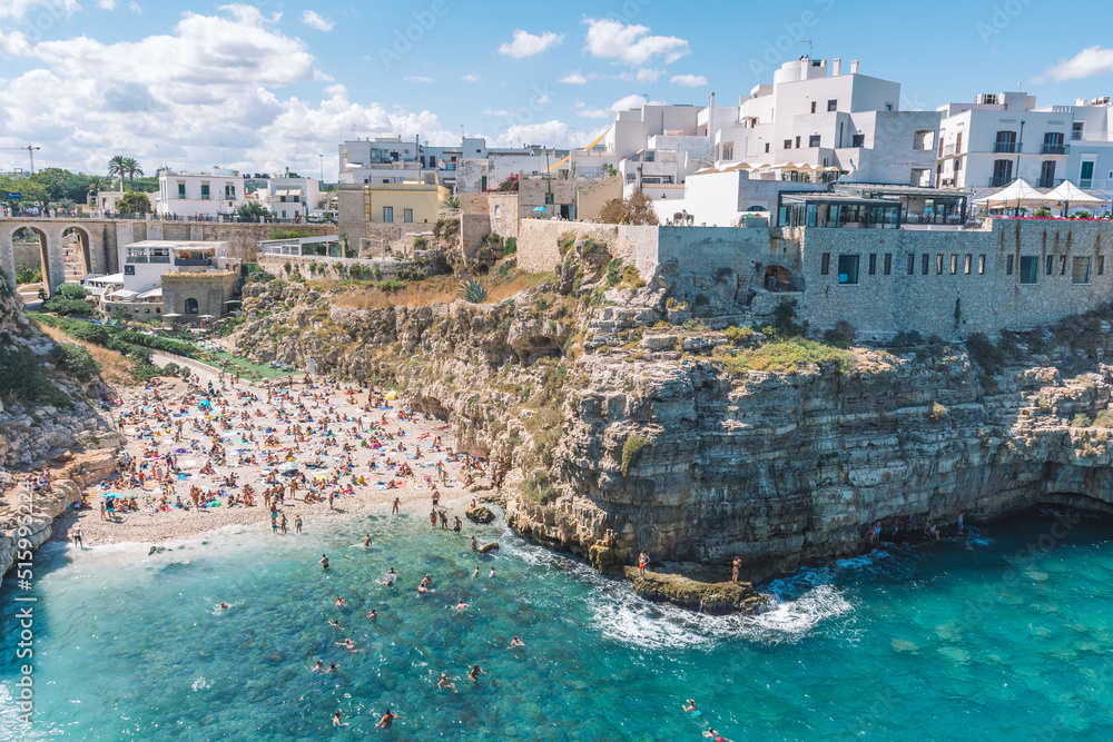 Beautiful aerial view of Polignano a Mare, Bari, Puglia, Italy, with white stone houses, cliff, beach, blue sea and bathers surrounded by Mediterranean nature