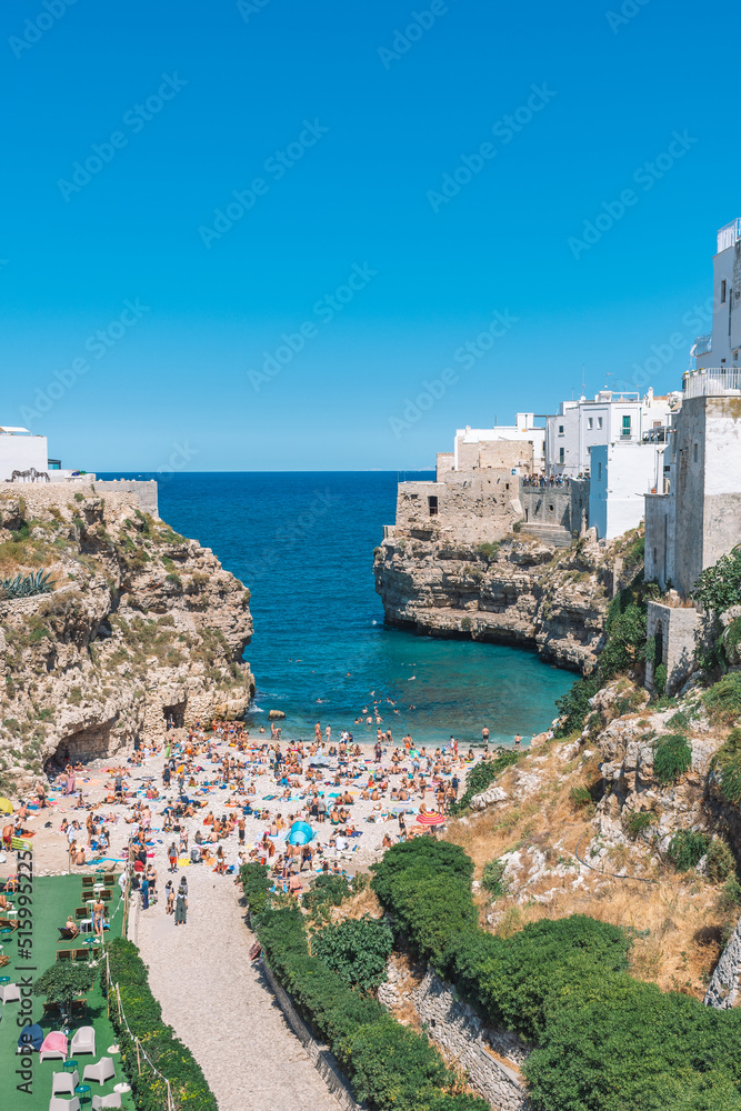 Beautiful aerial view of Polignano a Mare, Bari, Puglia, Italy, with white stone houses, cliff, beach, blue sea and bathers surrounded by Mediterranean nature, vertical Beautiful aerial view of Polignano a Mare, Bari, Puglia, Italy, with white stone houses, cliff, beach, blue sea and bathers surrounded by Mediterranean nature, vertical