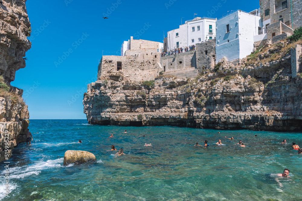 Beautiful view of Polignano a Mare with white stone houses, cliff, beach, blue sea and bathers surrounded by Mediterranean nature