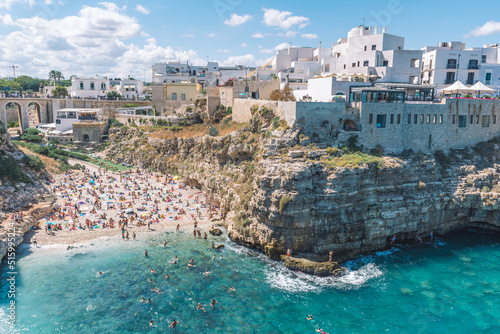 Beautiful aerial view of Polignano a Mare, Bari, Puglia, Italy, with white stone houses, cliff, beach, blue sea and bathers surrounded by Mediterranean nature