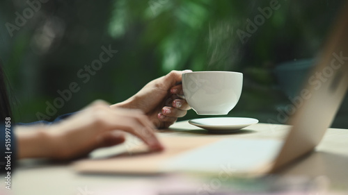 Cropped image of young woman hand holding cup of hot coffee with natural morning background