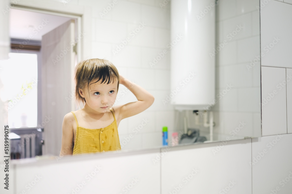 Cute toddler baby combs in front of bathroom mirror Cute toddler baby combs in front of bathroom mirror