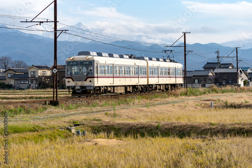 雪をいただく山を背に、のどかな田園風景の中を走る富山地方鉄道の電車 photo