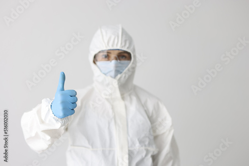 Woman in protective respirator and white coverall showing thumb up sign photo