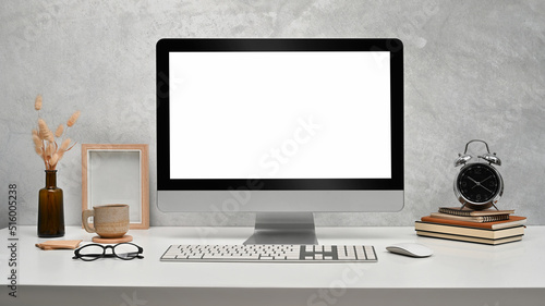 Front view computer with empty display, picture frame, books and alarm clock on white table