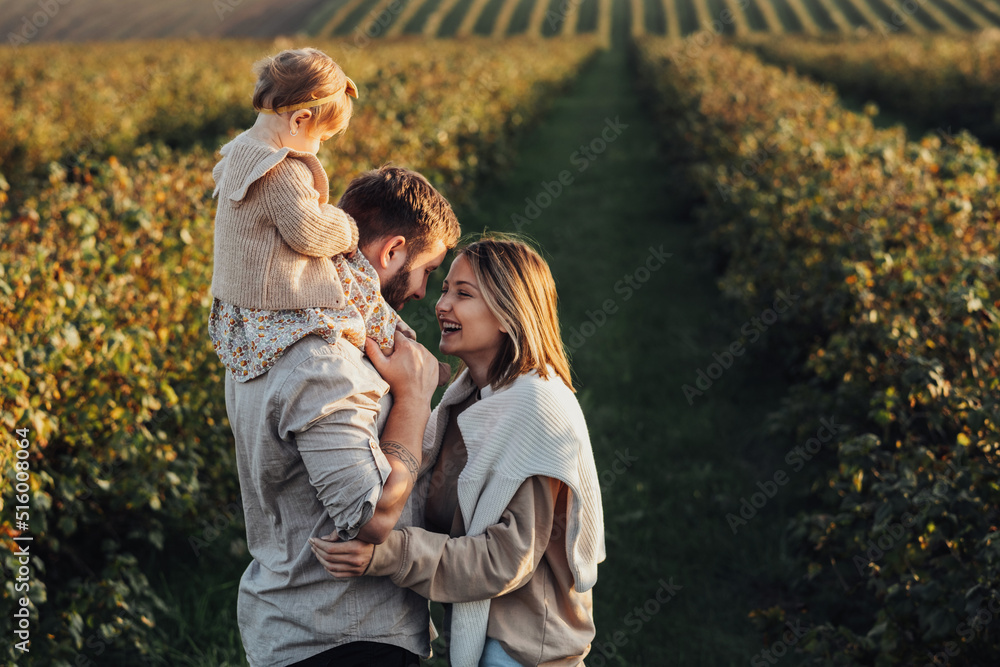 Happy Young Family Outdoors, Mother and Father with Their Baby Daughter at Sunset in the Field