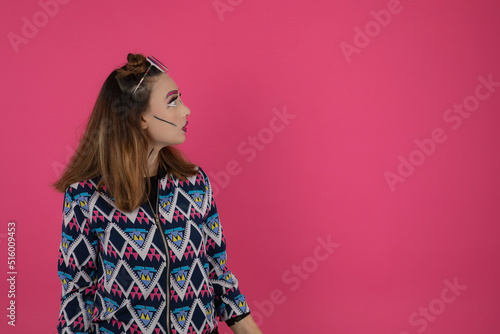 Portrait of young girl wearing colorful fantasy makeup and looking aside. Youn girl on pink background