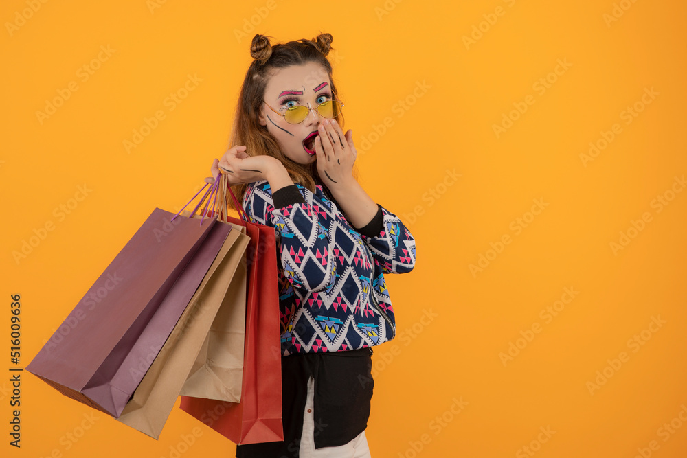 Creative beautiful girl holding shopping bags and put hand to her mouth while looking at camera Creative beautiful girl holding shopping bags and put hand to her mouth while looking at camera