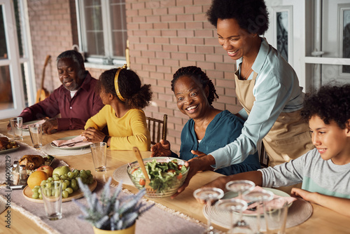 Happy black woman serving food at dining table during family lunch on patio.