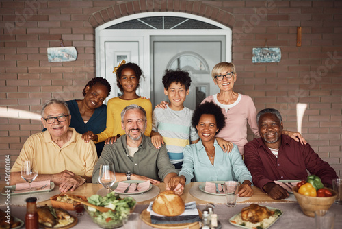 Portrait of happy multiethnic extended family at dining table on patio looking at camera.