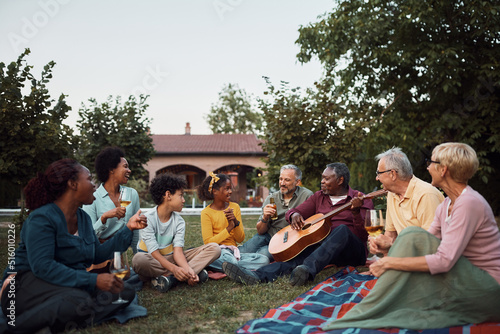 Happy multiracial extended family enjoying in drinks and acoustic music in backyard.