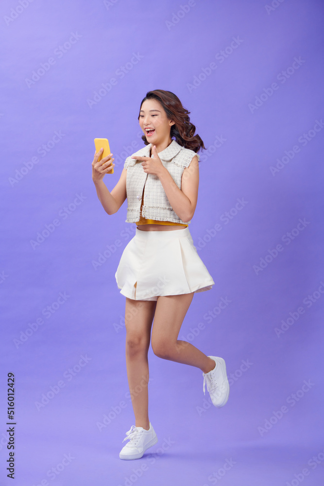 excited woman pointing with finger at smartphone and jumping on purple background excited woman pointing with finger at smartphone and jumping on purple background