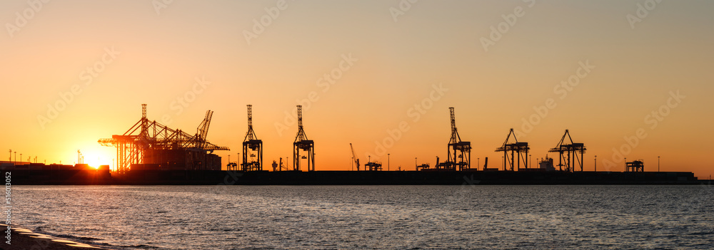 Harbor in Gdansk with commercial dock and cranes during sunset. Panoramic view from Stogi beach in Baltic sea. Silhouette of industrial port Harbor in Gdansk with commercial dock and cranes during sunset. Panoramic view from Stogi beach in Baltic sea. Silhouette of industrial port