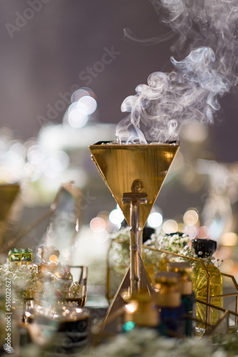 Oud (Agar wood chips with musky scent) burning in a gold Mabkhara (censer) on a table with perfume bottles and Baby's Breath at an Arabic wedding.