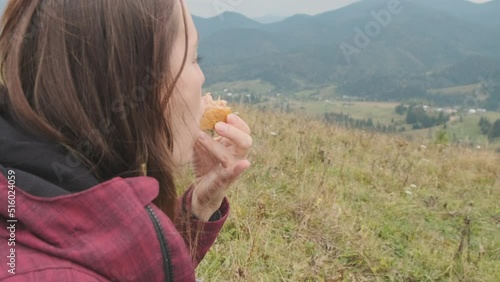 Young tourist feamle eating sandwich with tuna. Close-up, face, beautiful view mountains, green forest, clouds, nature. Backpacker's halt. The concept of travel, replenishment of strength, energy. photo