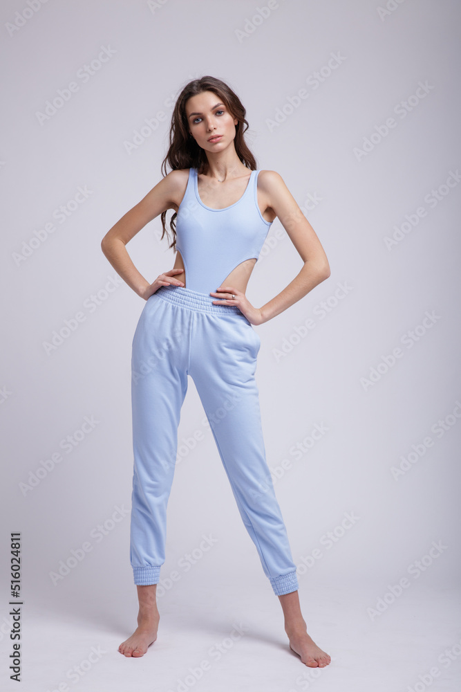High fashion photo of a beautiful elegant young woman in a pretty blue body slim, pants posing on white background. Slim figure, studio shot. Brunette, long hair High fashion photo of a beautiful elegant young woman in a pretty blue body slim, pants posing on white background. Slim figure, studio shot. Brunette, long hair