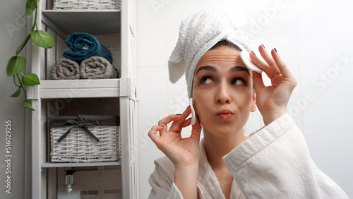 Cute funny girl cleaning face with cotton pads. Woman removing makeup. Home bathroom beauty treatment.