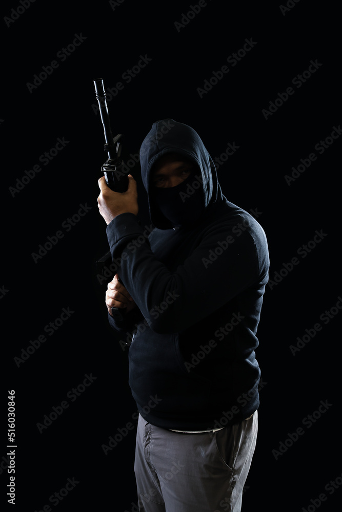 Portrait of a terrorist wearing a black hoodie holding a m16 rifle on a black background.concept of terrorism. Portrait of a terrorist wearing a black hoodie holding a m16 rifle on a black background.concept of terrorism.
