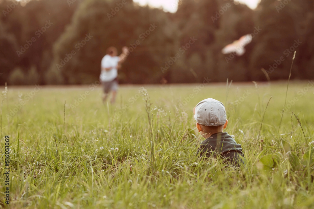 Family vacation. Summer outdoor photo of a father and son flying a kite in a meadow. A picture against the sun. Warm family moments or a conceptual image for spending time outdoors. Family vacation. Summer outdoor photo of a father and son flying a kite in a meadow. A picture against the sun. Warm family moments or a conceptual image for spending time outdoors.