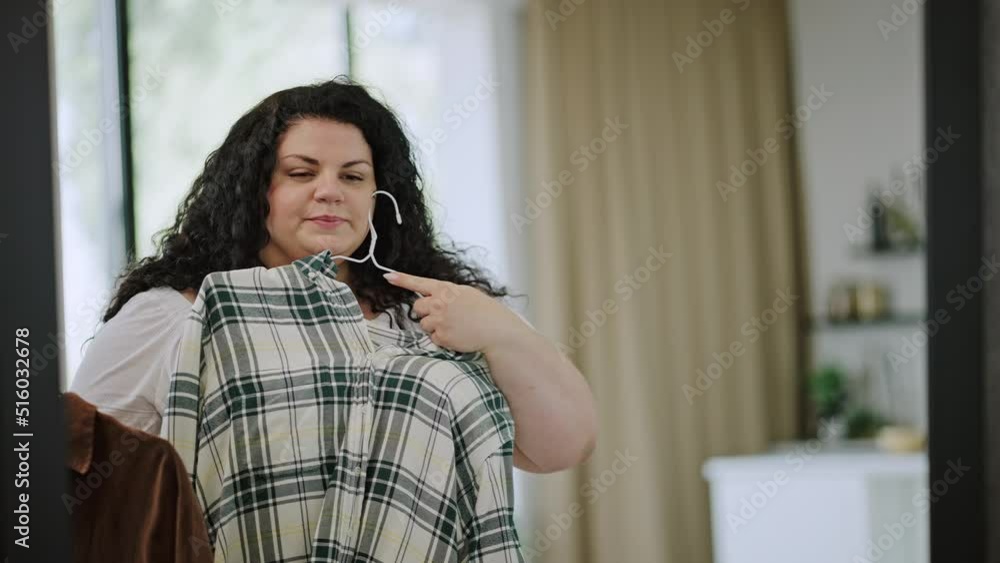 Young overweight woman gets ready for walk choosing blouses Young overweight woman gets ready for walk choosing blouses