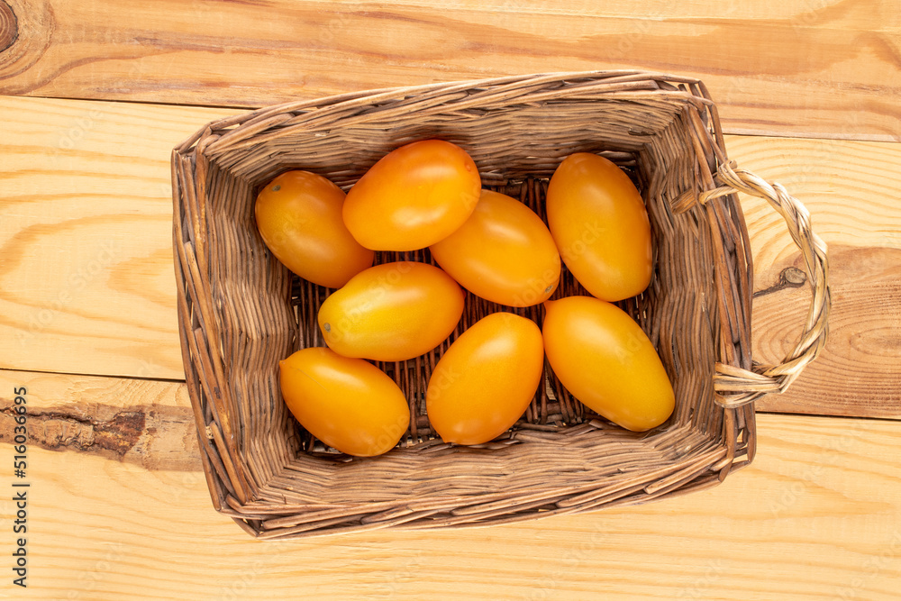 Several ripe yellow tomatoes in a basket on a wooden table, close-up, top view. Several ripe yellow tomatoes in a basket on a wooden table, close-up, top view.