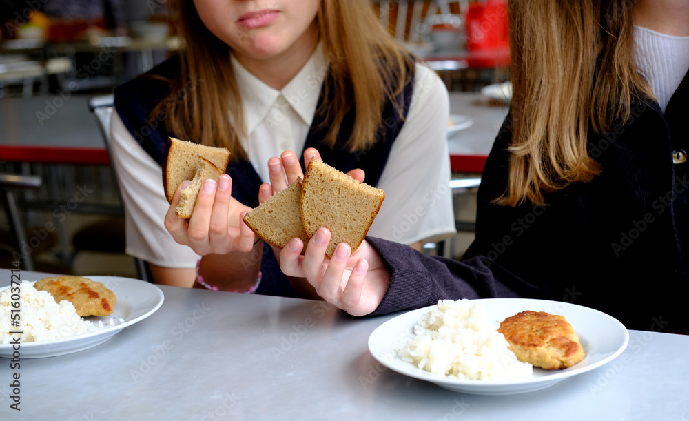The concept of the problem in school meals. Two schoolgirl girls hold bread in their hands and look at the food with displeasure.
