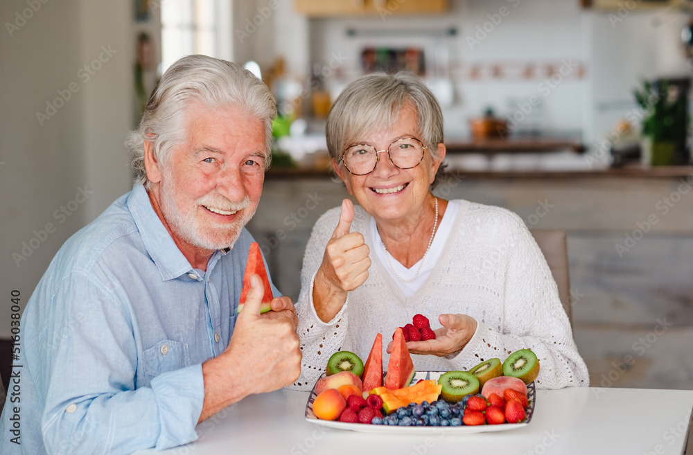 Happy beautiful retired senior couple having break with fresh seasonal fruit at home, thumb up looking at camera, healthy eating concept Happy beautiful retired senior couple having break with fresh seasonal fruit at home, thumb up looking at camera, healthy eating concept
