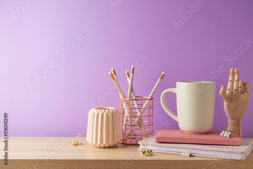 Stylish feminine table with coffee cup, notebook and pencils over purple background. Back to school concept